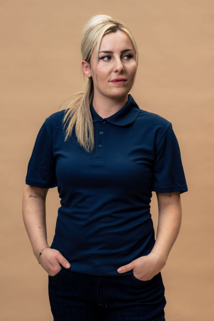 Model draagt Polo Lennox circulaire polo donkerblauw en kijkt naar rechts met handen in de broekzakken.